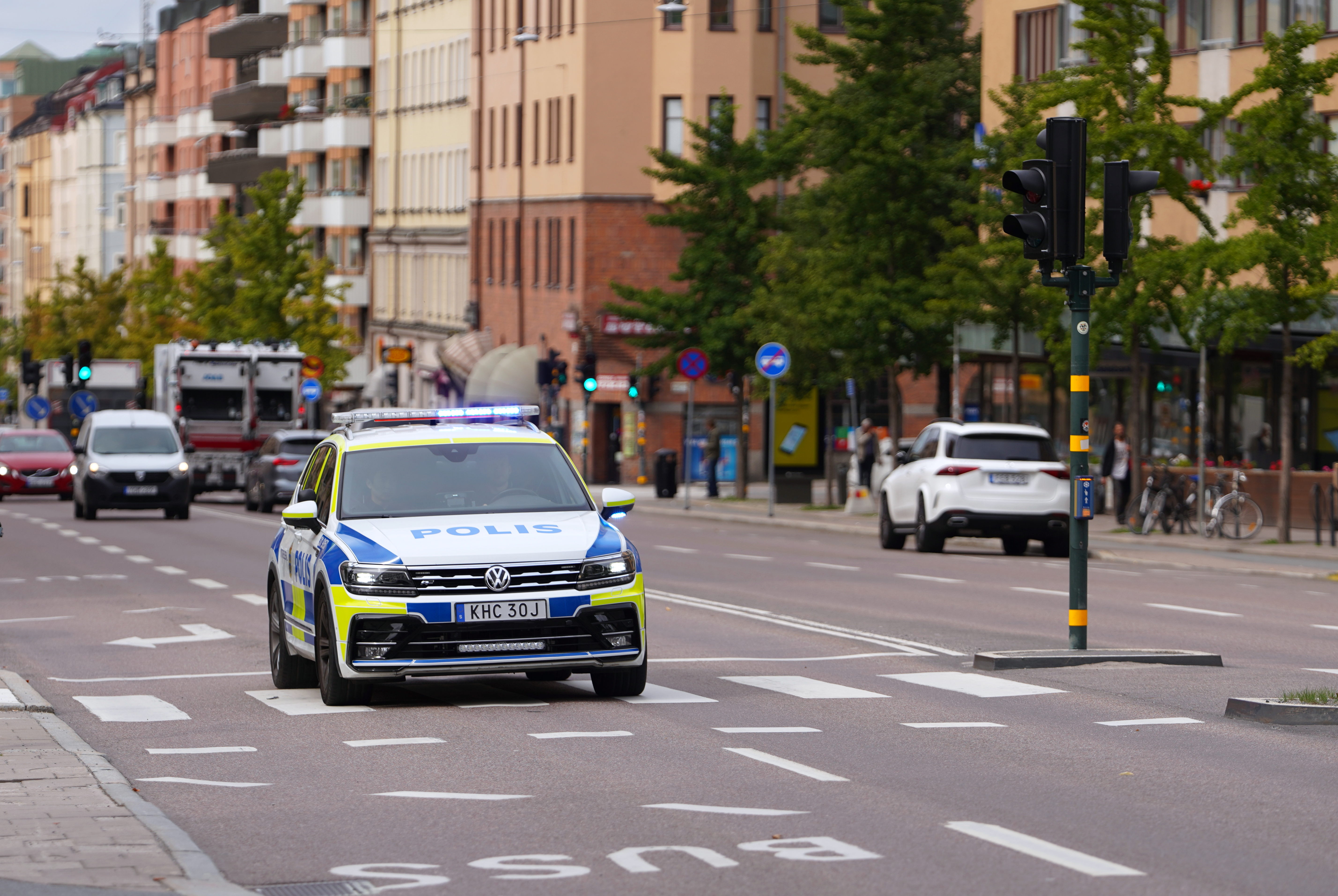 En svensk polisbil med blåljus påslaget kör längs en gata i en stad